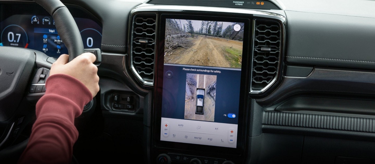 A driver using the backup camera on a Ford vehicle's infotainment screen to assist with parking.