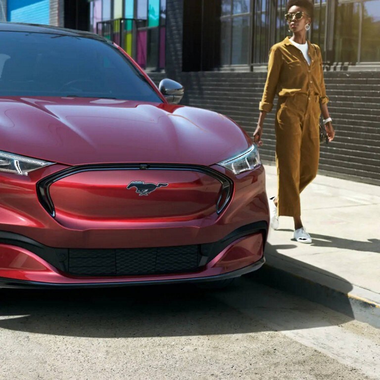 A woman standing next to a red Mustang Mach E