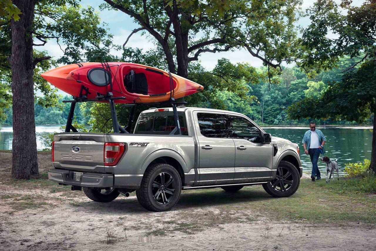 An f 1 50 parked by a lake with 2 kayaks mounted on a bed racks