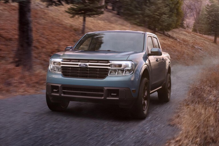 2022 Ford® Maverick LARIAT painted in Area 51 with available FX4 Off-Road Package driving down an evergreen-lined road at dusk