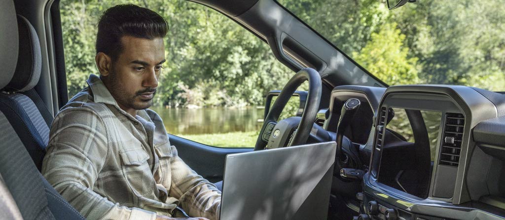 Person sitting in a 2025 Ford F-150® cab working on a laptop computer using the Interior Work Surface
