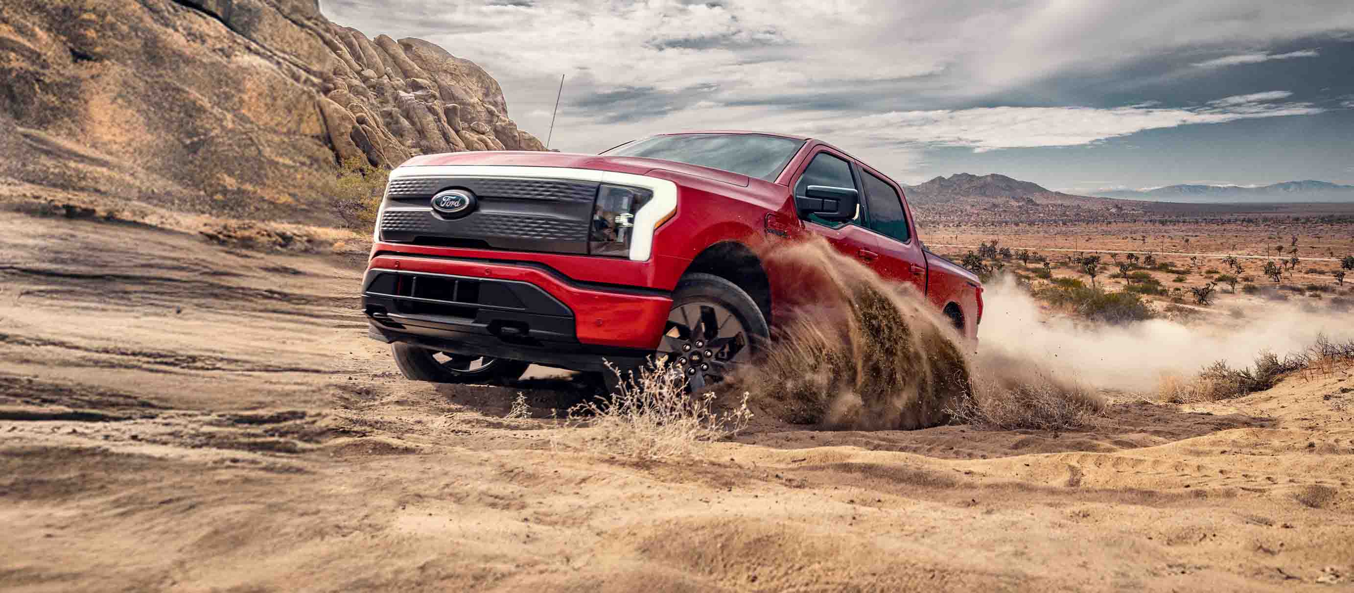 An F-150 Lightning driving through rough, sandy terrain.