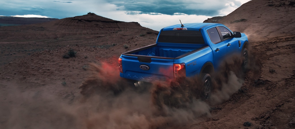 Rear view of a 2025 Ford Ranger® pickup being driven off, kicking up dust