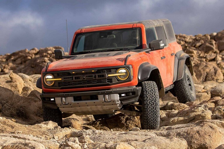 Four-door 2023 Ford Bronco® Raptor® in Hot Pepper Red Metallic Tinted Clearcoat being driven over rocks