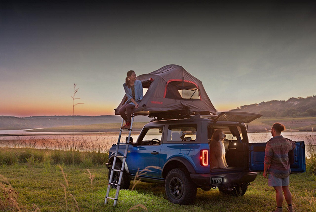 A couple setting up camp with a 2024 Ford Bronco® SUV with roof-mounted tent