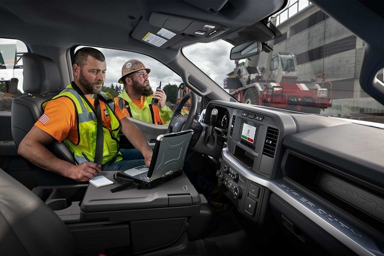 Worker using tablet inside a 2023 Ford Super Duty® Chassis Cab while other worker talks on a walkie talkie
