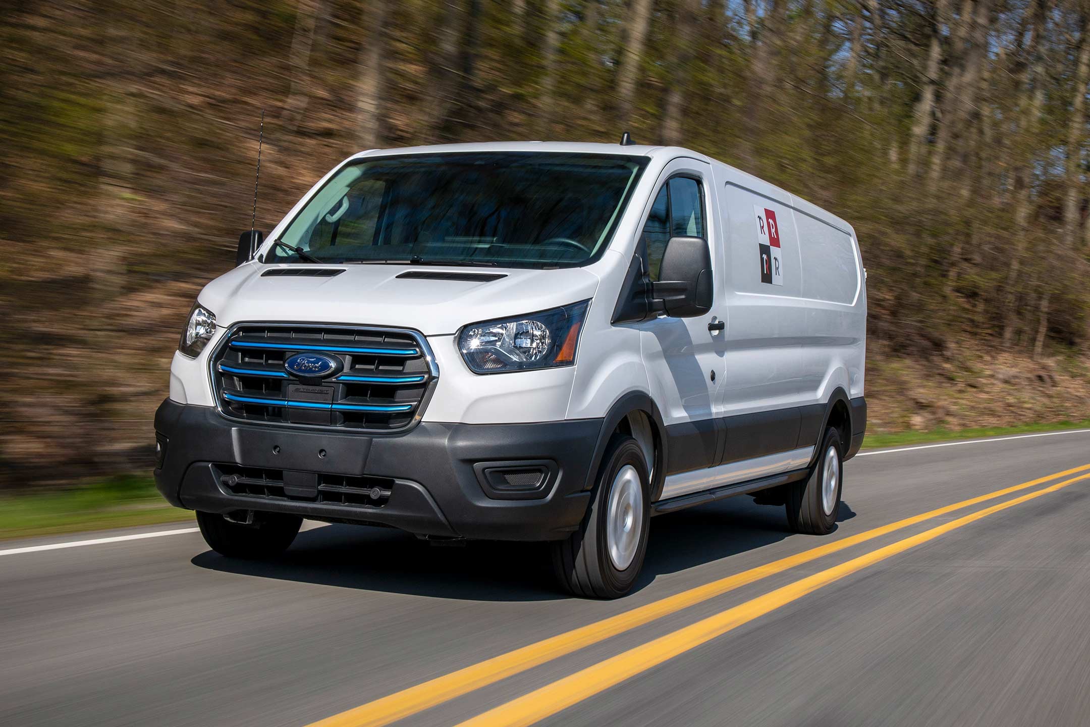 A white e transit cargo van drives along a two lane highway