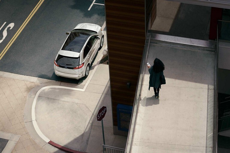Woman holds a smartphone on a walkway overlooking her 2024 Ford Edge® parked on the street below