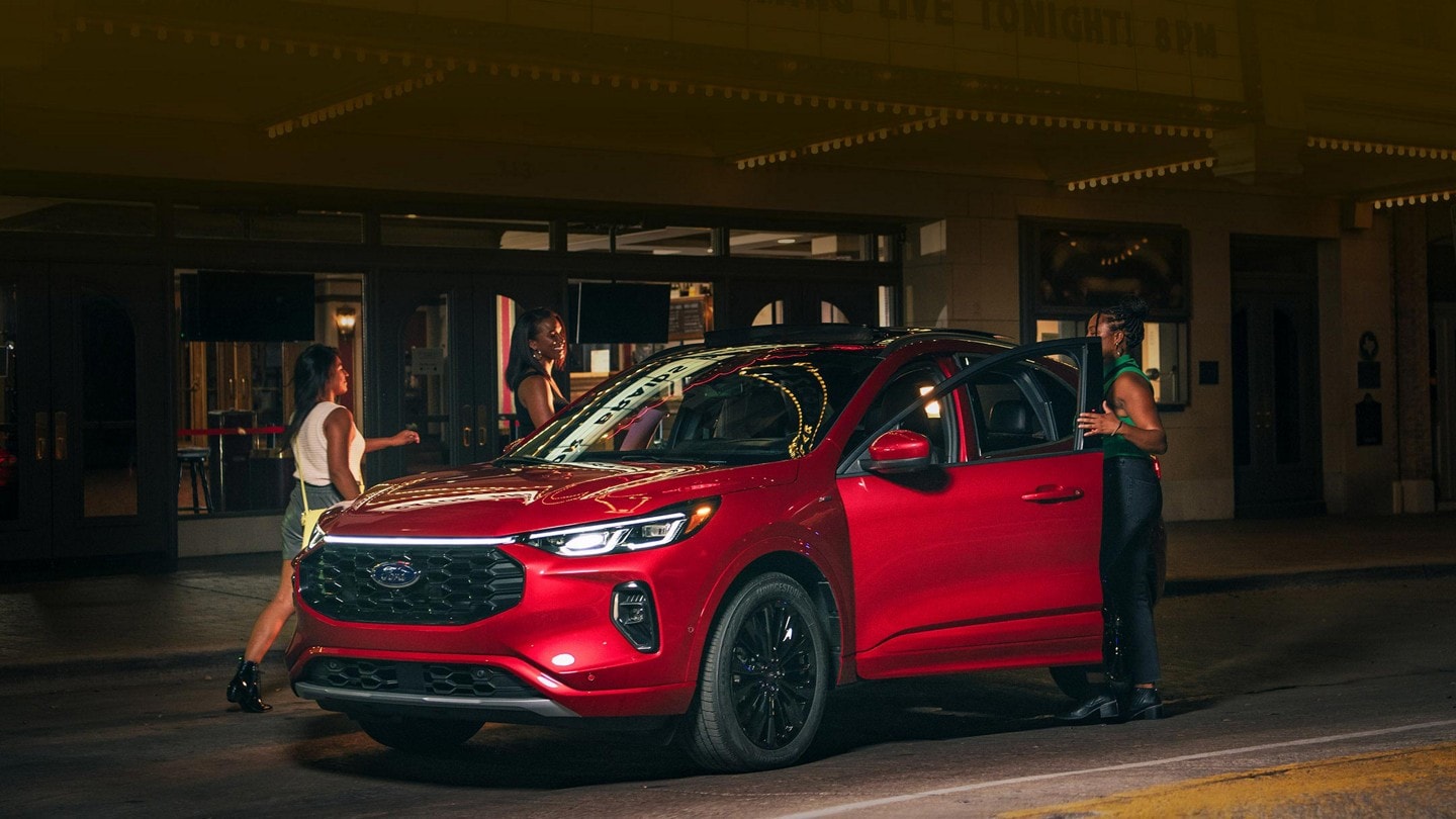 A 2023 Ford Escape® at night parked in front of a theatre and a woman getting in