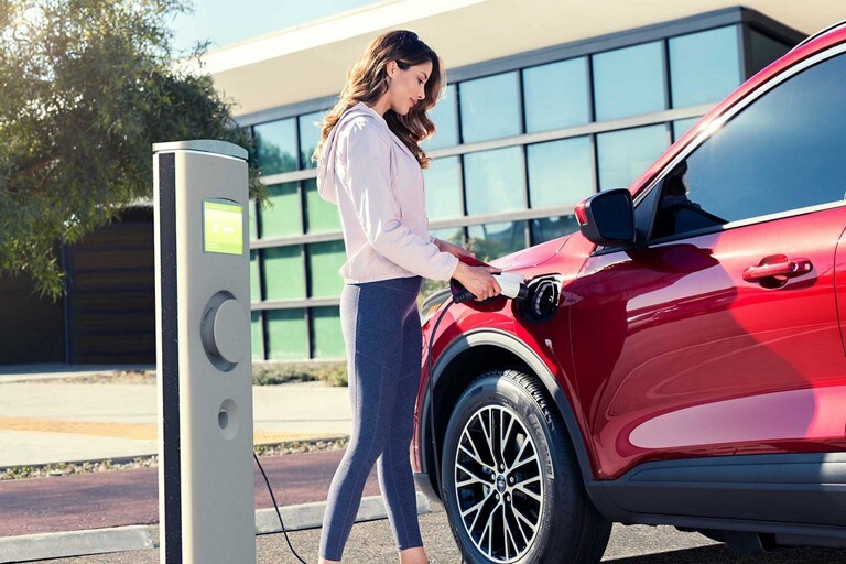 Person at a public station charging a 2024 Ford Escape® Plug-in Hybrid in Rapid Red Metallic Tinted Clearcoat