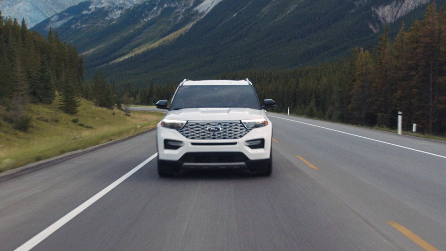 A white 2023 Ford Explorer drives toward the camera in a mountain highway setting