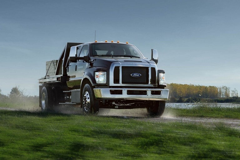 2023 Ford F-750 Crew Cab in Agate Black being driven on dirt road near grass and water