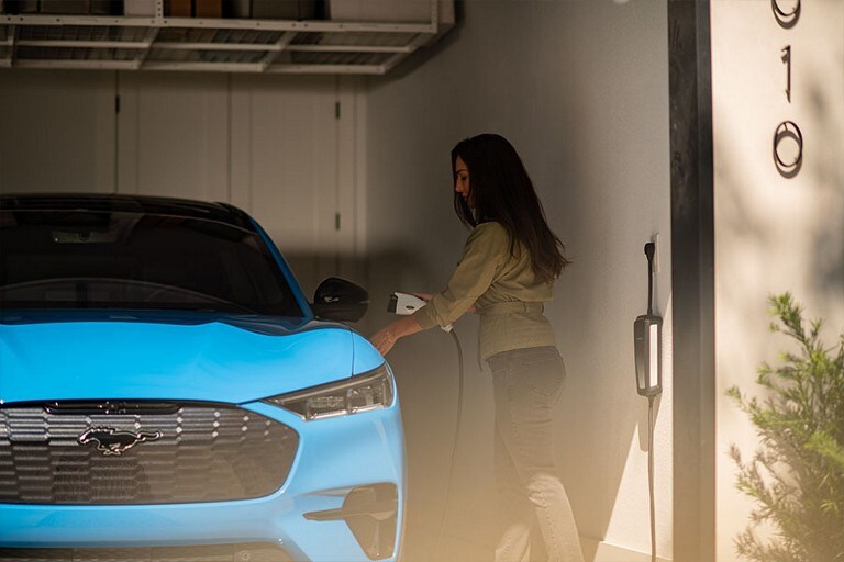 Woman in a garage holding a Ford Mobile Charger beside a 2023 Mustang Mach-E® SUV