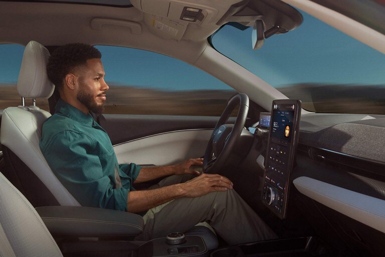 Man in a 2023 Ford Mustang Mach-E® SUV resting his hands on his knees as the vehicle is driven by Ford BlueCruise