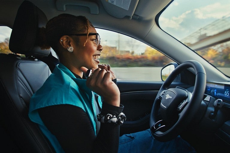 A woman in a 2024 Ford Mustang Mach-E® SUV sitting in the vehicle with her hands off the steering wheel
