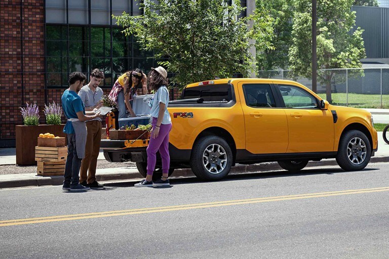 A group of friends are unloading plants from the bed of a 2023 Ford Maverick® while two men glance down at a tablet