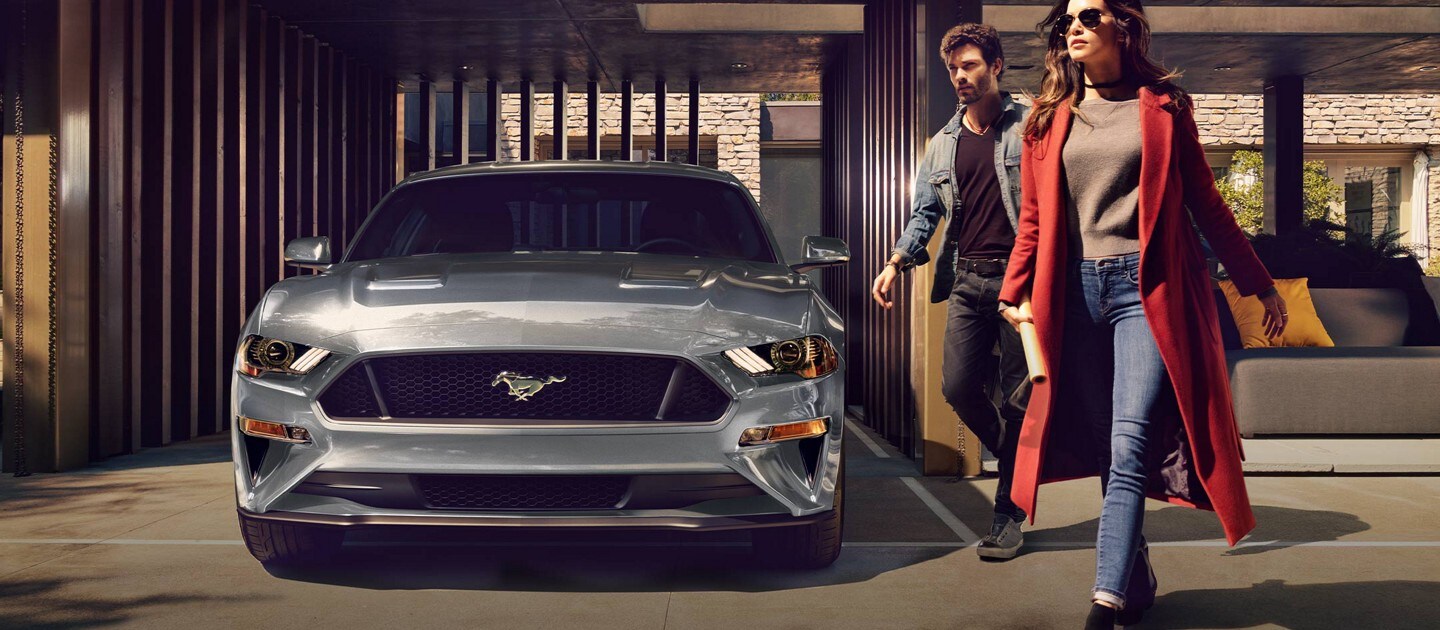 2023 Ford Mustang® coupe in Carbonized Grey Metallic parked in a carport with two people walking away