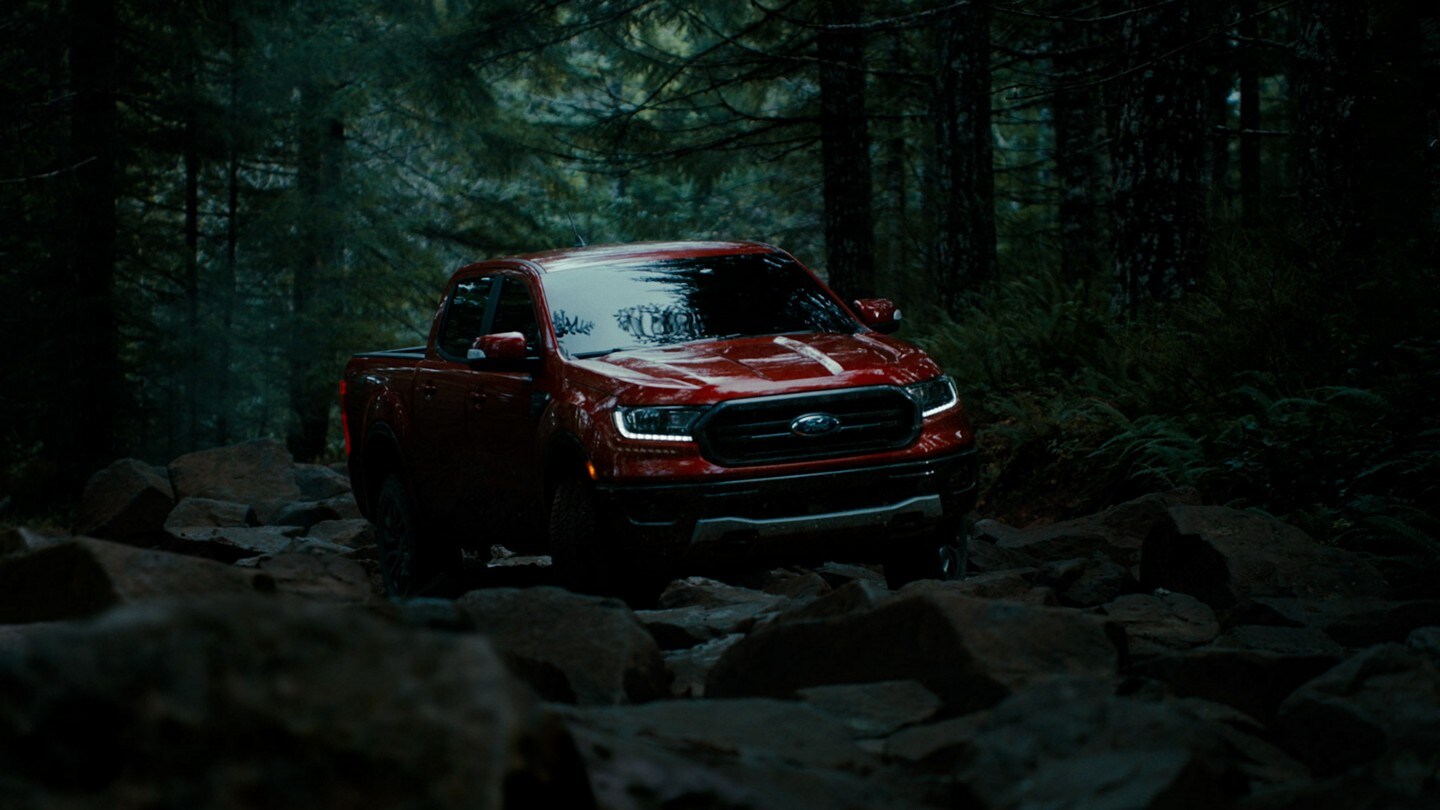 A red 2023 Ford Ranger crosses rocky ground in a wooded area
