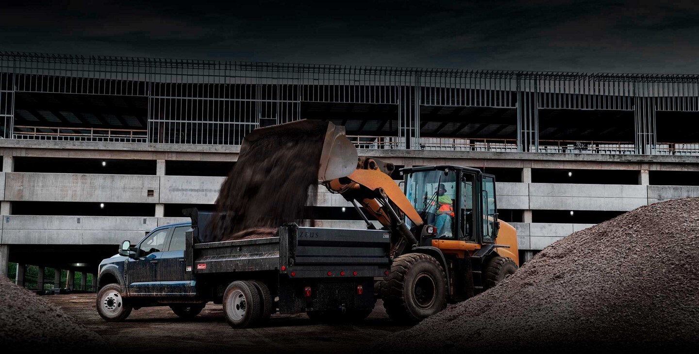 A backhoe dumping dirt into the bed of a 2023 Ford Super Duty® F-600®
