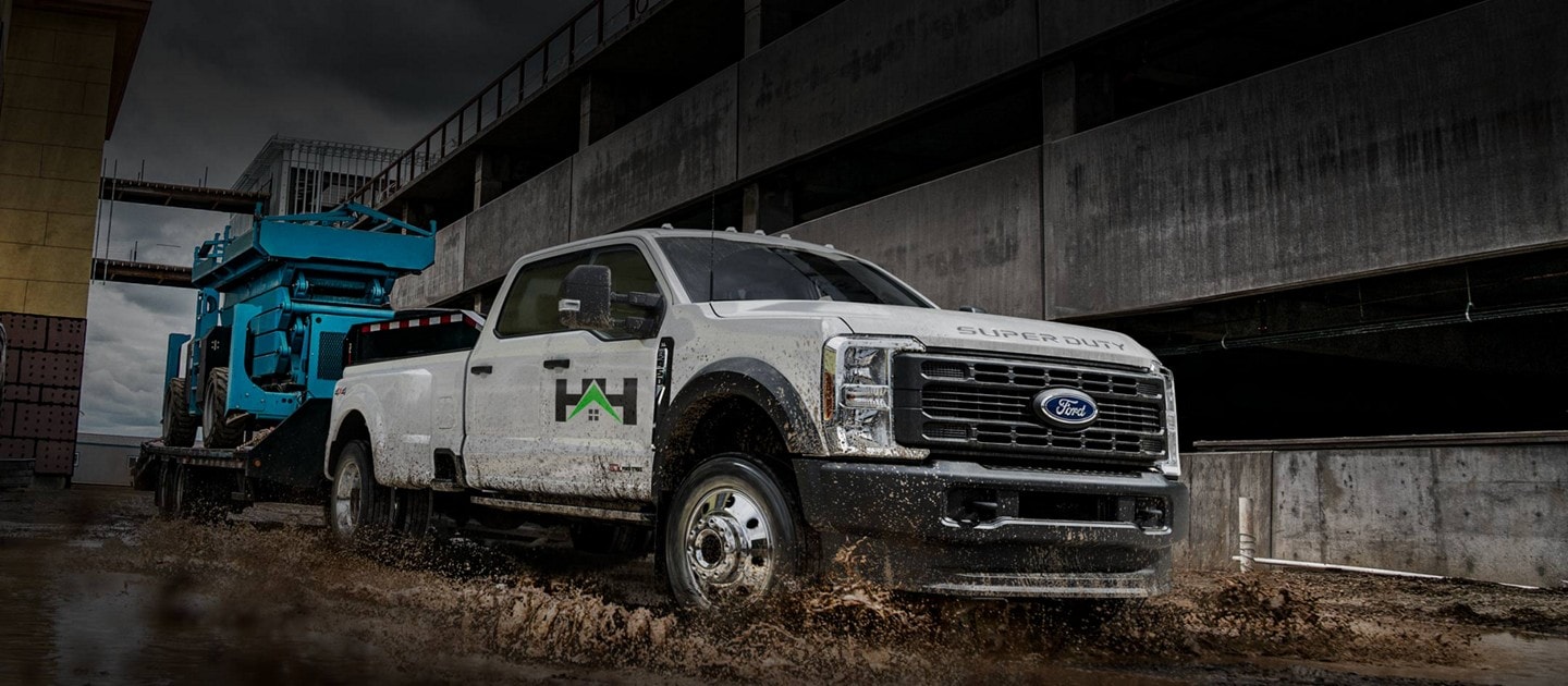 2025 Ford Super Duty® F-450® XL DWR truck in Oxford White pulling a hydraulic lift through a large puddle of mud