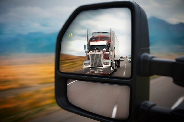 Close-up of the side view mirror with BLIS icon and reflection of a semi-truck