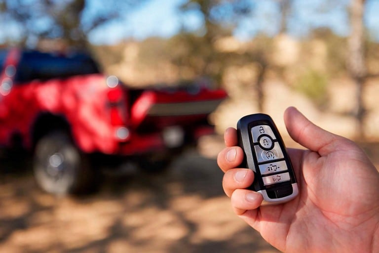Hand holding key fob with a red 2025 Ford Super Duty® King Ranch® pickup in the background