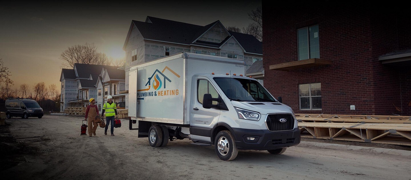 Two construction workers walking near a 2024 Ford Transit® Chassis Cab model with box truck upfit parked at a jobsite