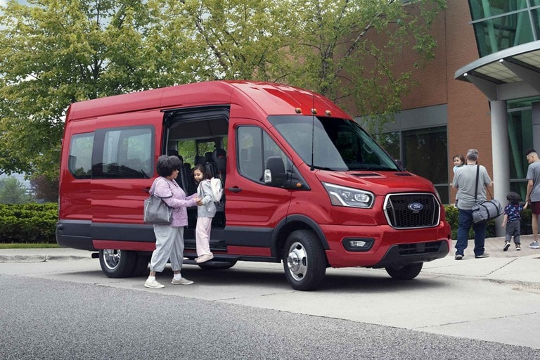 A woman helping a young girl out of the side door of a 2023 Ford Transit® van