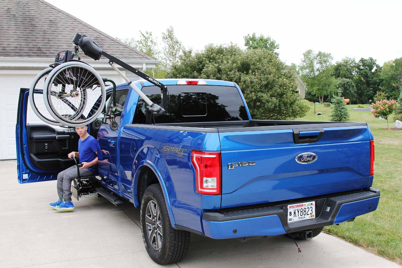 A blue F-150 with a wheelchair hoist in the bed.