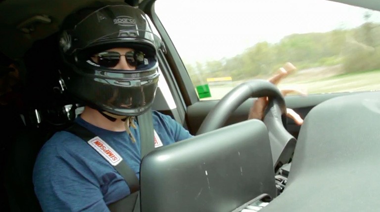 A racing driver wearing a helmet drives a Ford vehicle.