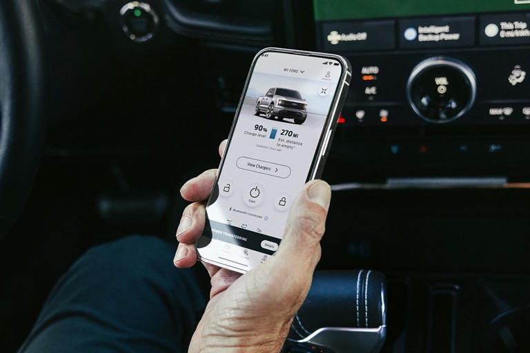 Person holding a smart phone displaying a vehicle’s charging status.