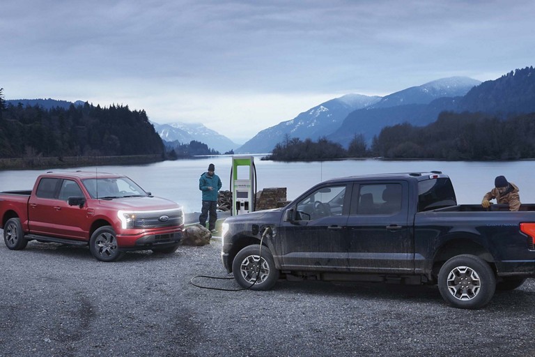 Two F-150 Lightning trucks parked and charging at a remote public charging station.