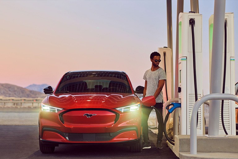 A man stands next to a red FOrd Mustang Mach E while it charges