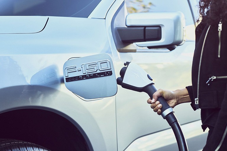 A hand inserts a cable into the charging port of a Ford F 1 50 Lightning