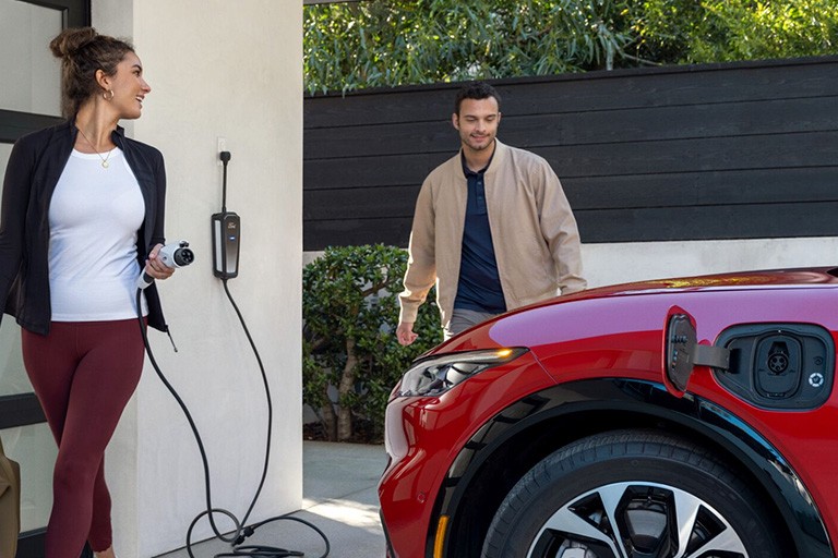 A woman holds a charging cable near a FOrd Mustang Mach E with its charging port open.