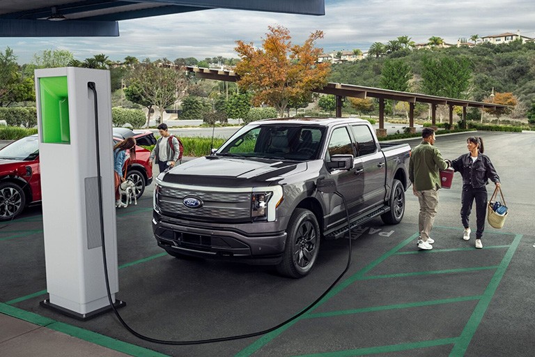 A couple stand next to a Ford F 1 50 Lightning parked at a D C fast charging station