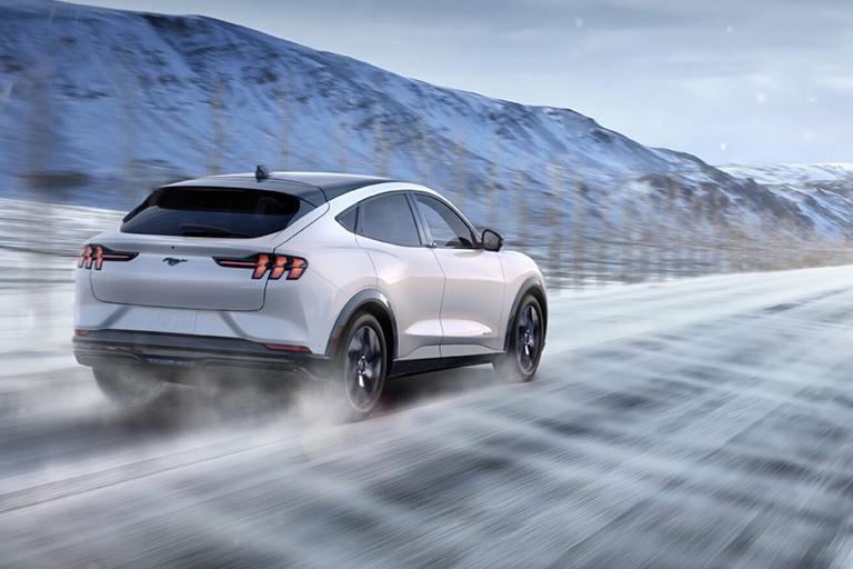 A Ford Mustang Mach E drives along a wintery highway