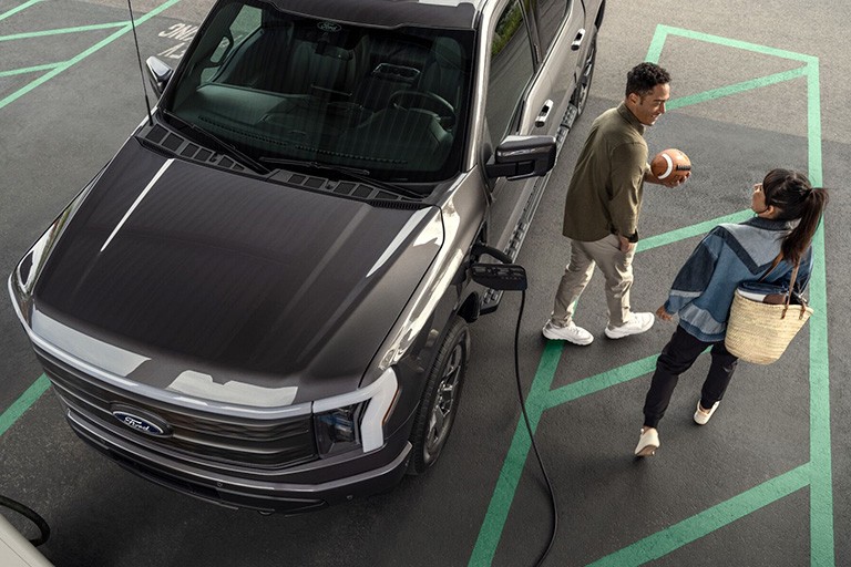A couple walk away from an F 1 50 Lightning parked at a charging station