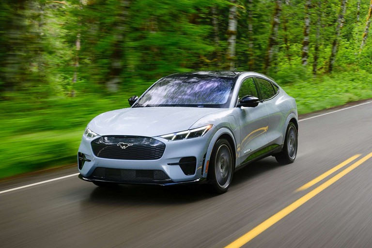 Mustang Mach-E driving on a tree-lined road.