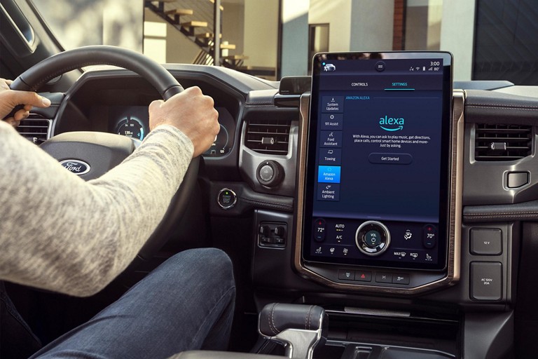 A person driving a Ford vehicle with the dashboard displaying Amazon Alexa.