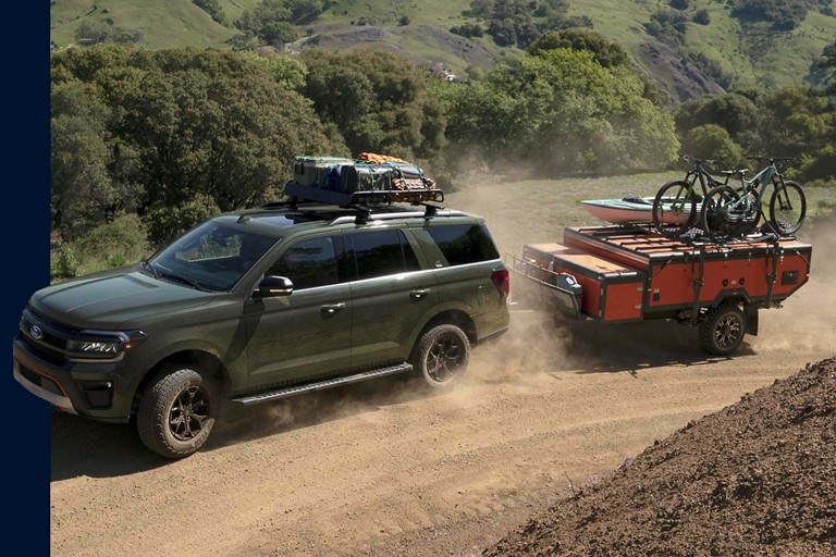 A Ford Expedition towing a trailer with mounted bikes and canoe.