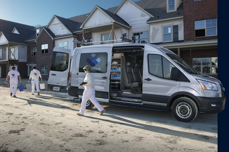 A Ford E-Transit commercial service van parked in front of a house.