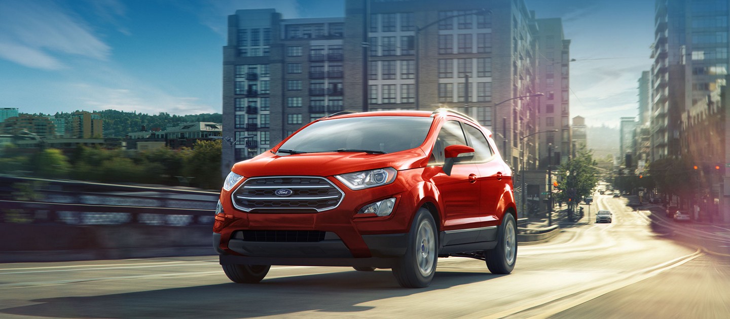 A red Ford EcoSport drives along a city street.