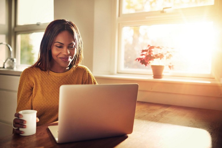 A woman looks at a laptop screen on the kitchen table