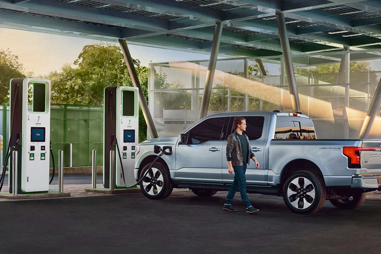 Person walks by an F-150 Lightning parked at a public charging station.