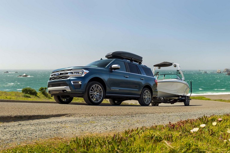 A Ford SUV towing a boat on a coastal road.