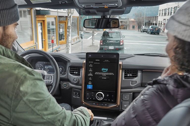 Driver and passenger in a Ford vehicle with the Alexa logo appearing on the display.