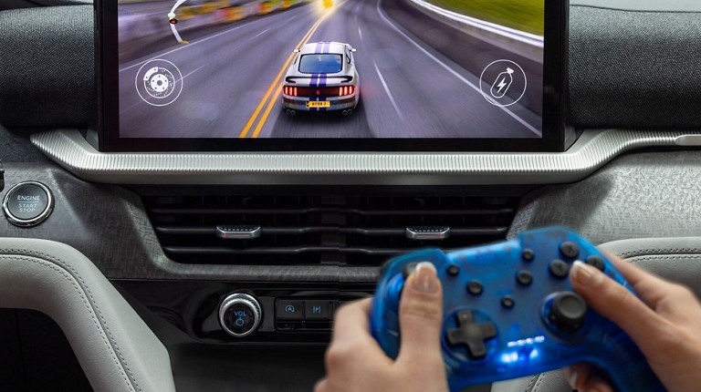 A passenger holding a game control and playing a car racing game on the vehicle screen in a parked Ford SUV. Screen may vary.