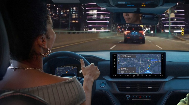 A driver in a Ford SUV on a city highway at night while using the vehicle screen’s navigation system. Screen may vary.