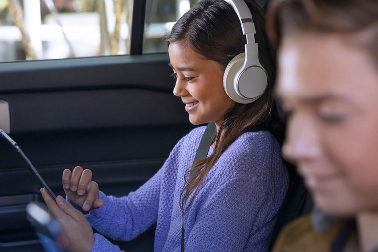 Two smiling children using mobile devices while sitting in the second and third rows of a Ford SUV.